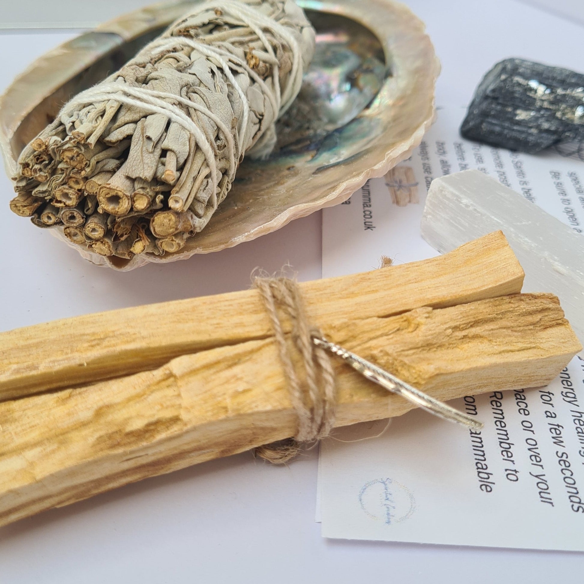 close up of the sage in the abalone shell. Palo santo in the foreground and selenite and tourmaline next to it