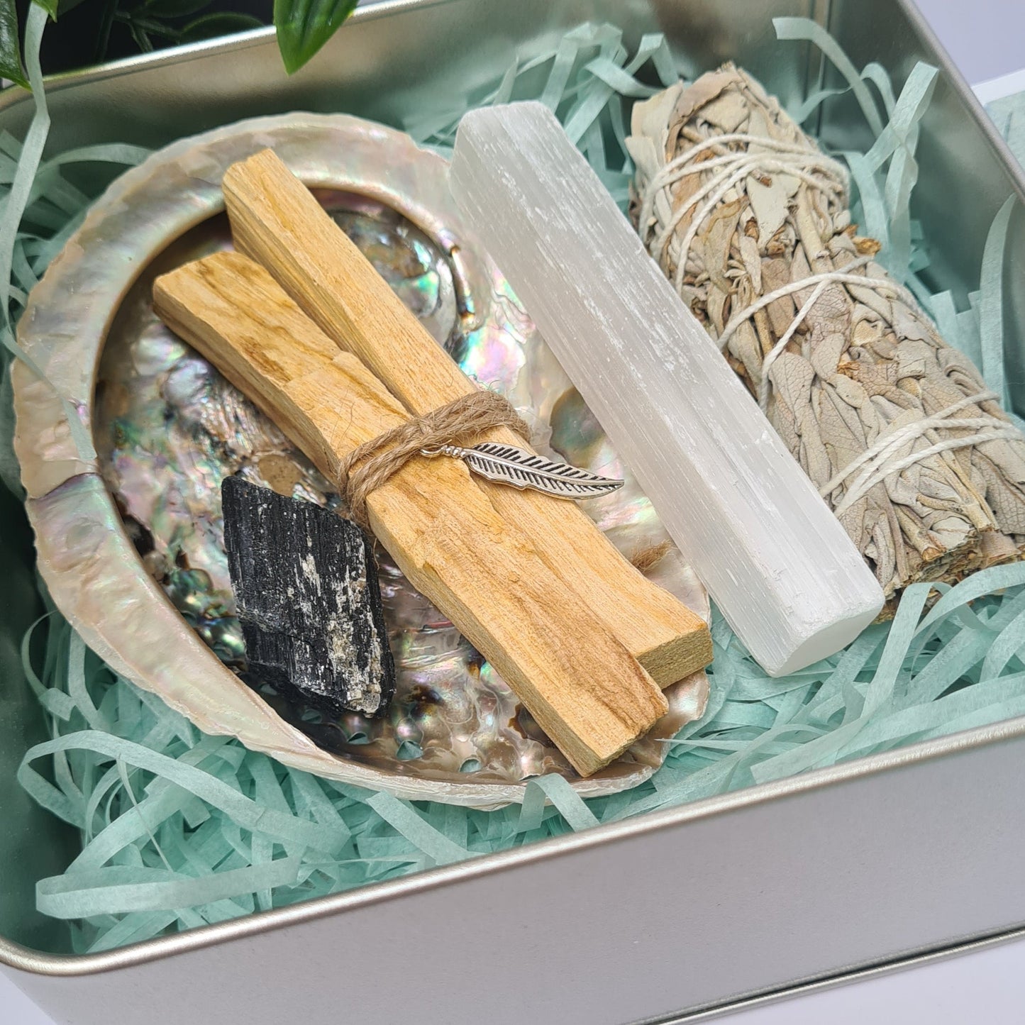 Energy cleansing kit with sage, tourmaline, selenite, palo santo, and abalone shell neatly arranged in a reusable tin box.