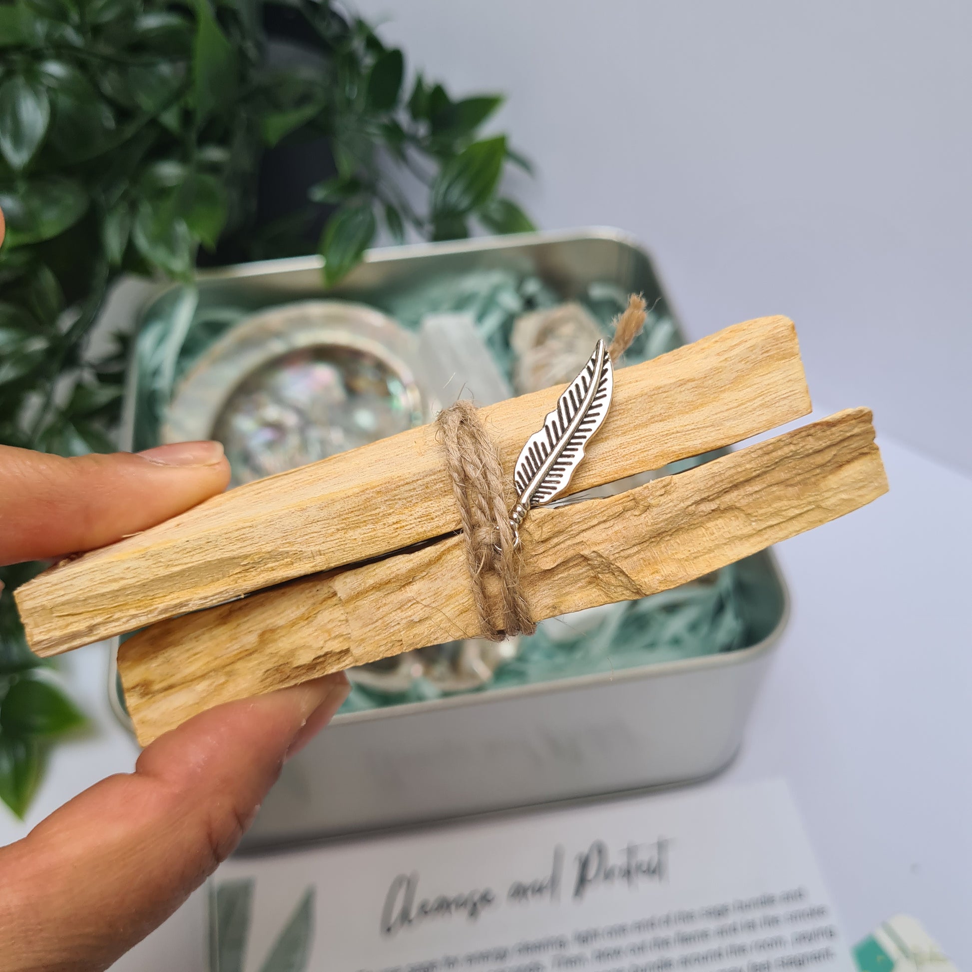 Hand holding a palo santo bundle of 2 sticks tied with twine with a feather charm