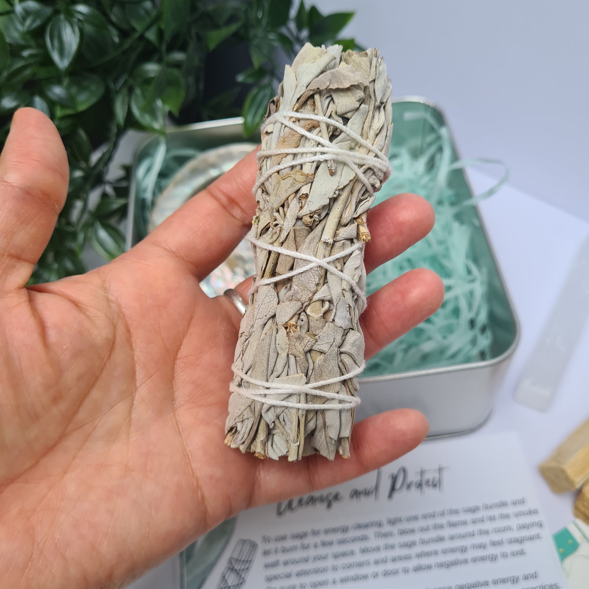 hand holding a sage bundle with tin in background